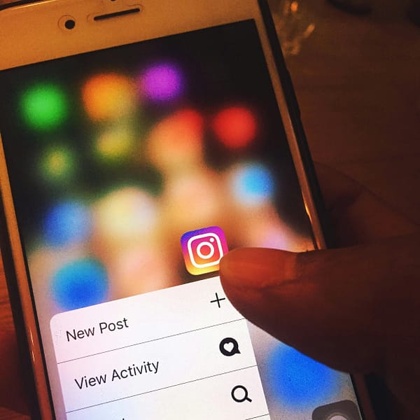 Finger navigating Instagram app on a smartphone screen with colorful blurred background.